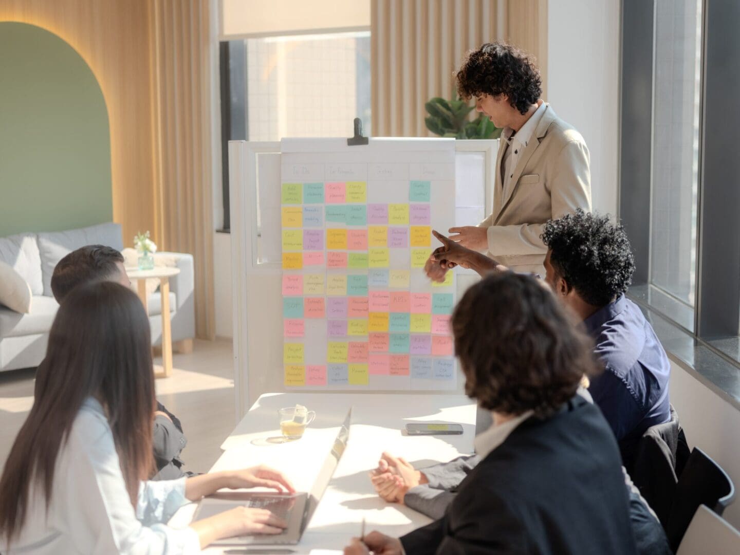 Diverse group of professionals brainstorming and collaborating together in a modern, bright office setting with whiteboard and sticky notes