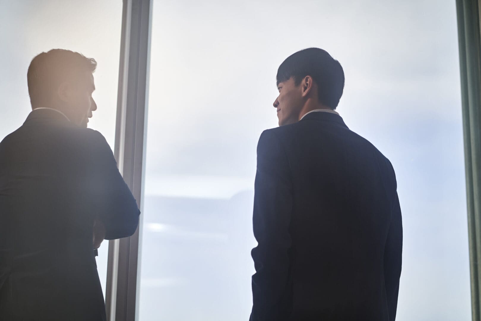 two asian business people colleage standing by the window talking chatting discussing while looking at city view in office