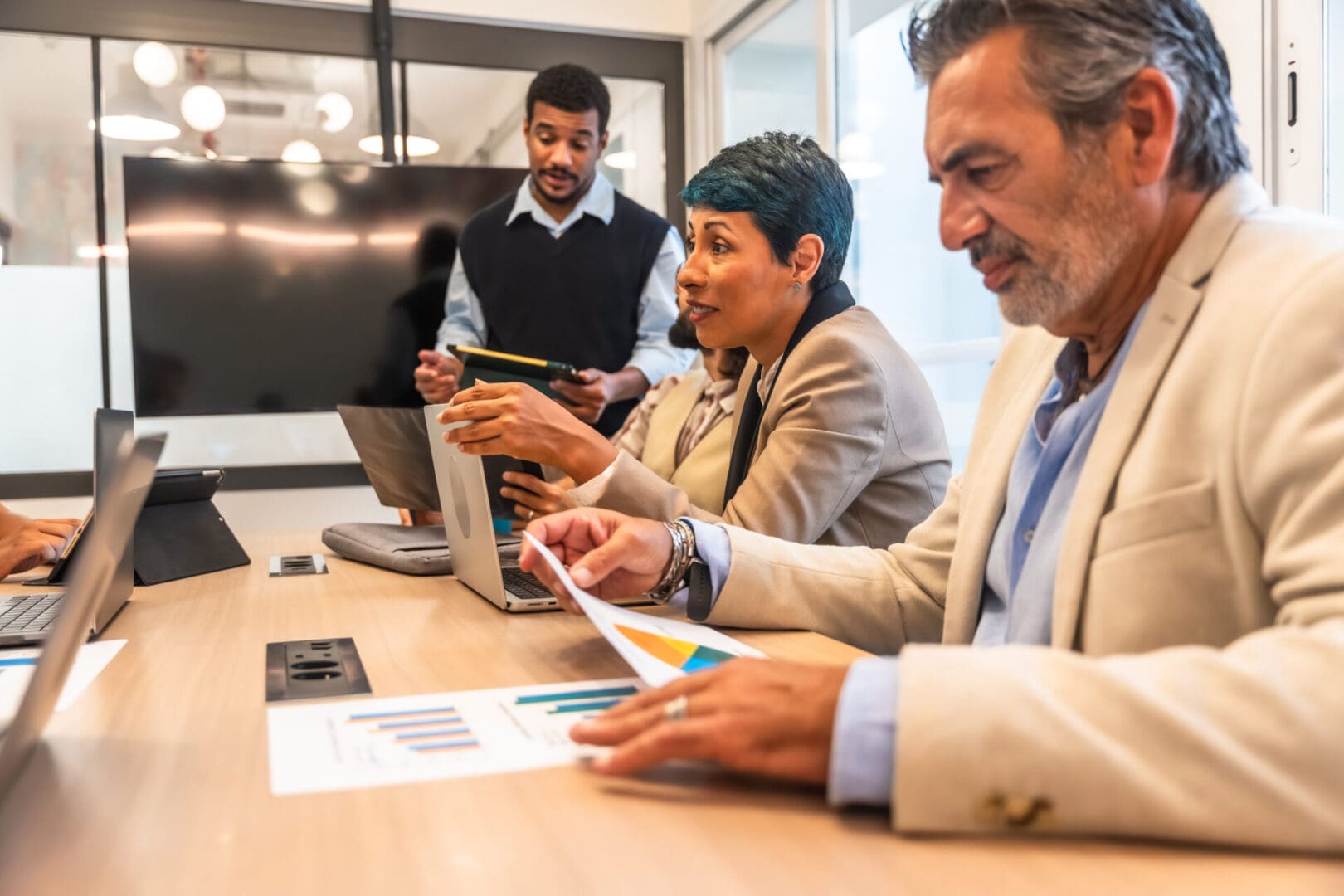 Diverse professionals collaborating in a modern conference room, reviewing charts and data on laptops and tablets, discussing strategy and teamwork for business growth and planning