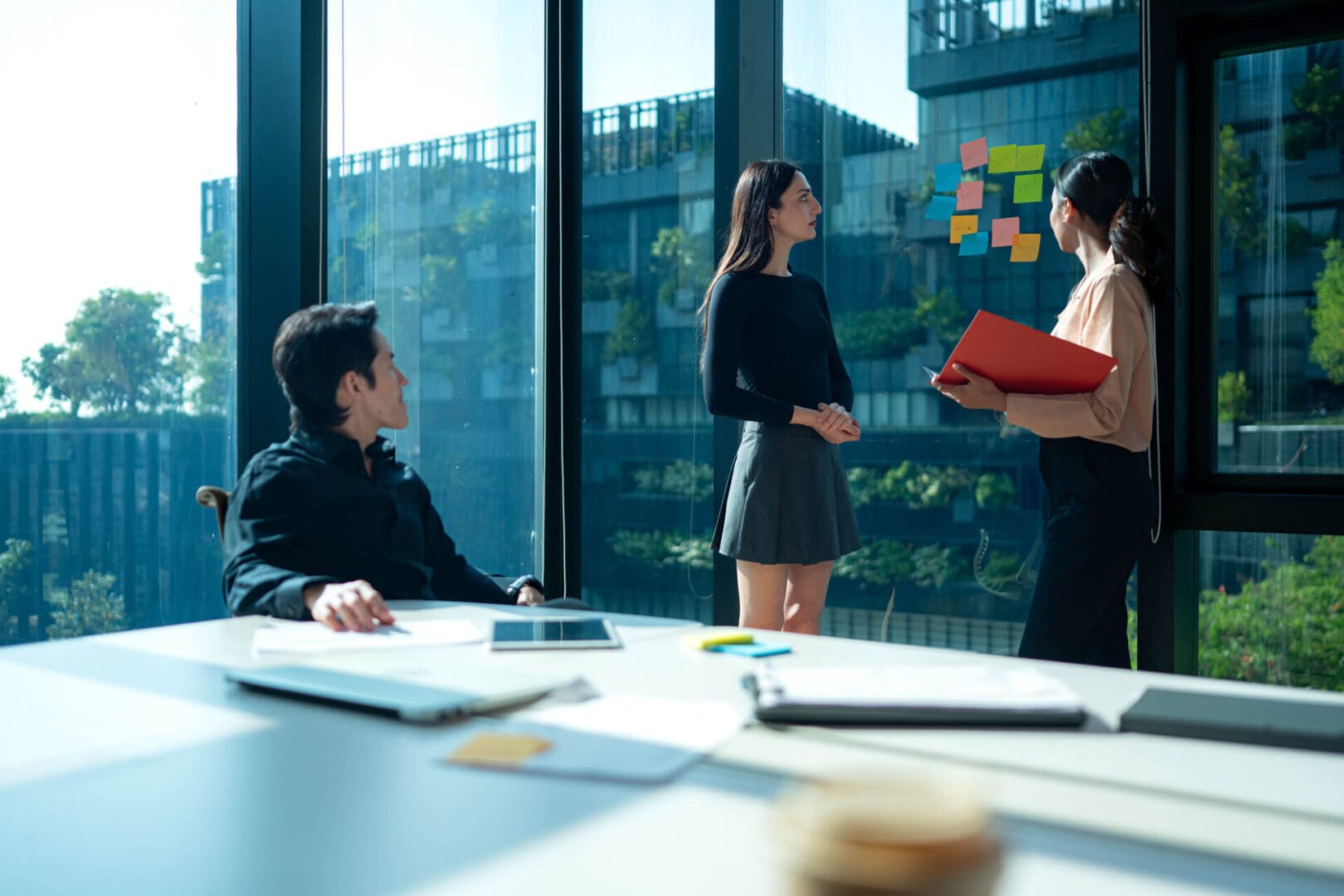 Business team discussing ideas while looking at colorful sticky notes on a glass window in a modern office meeting room