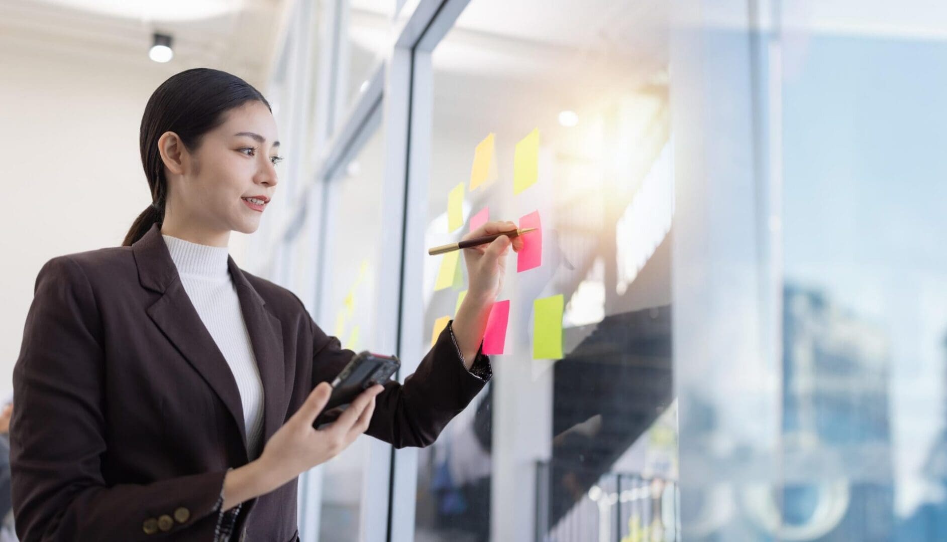 Brainstorming and at idea notes concept, Business woman looking at sticky note on glass wall and sharing ideas in the office.
