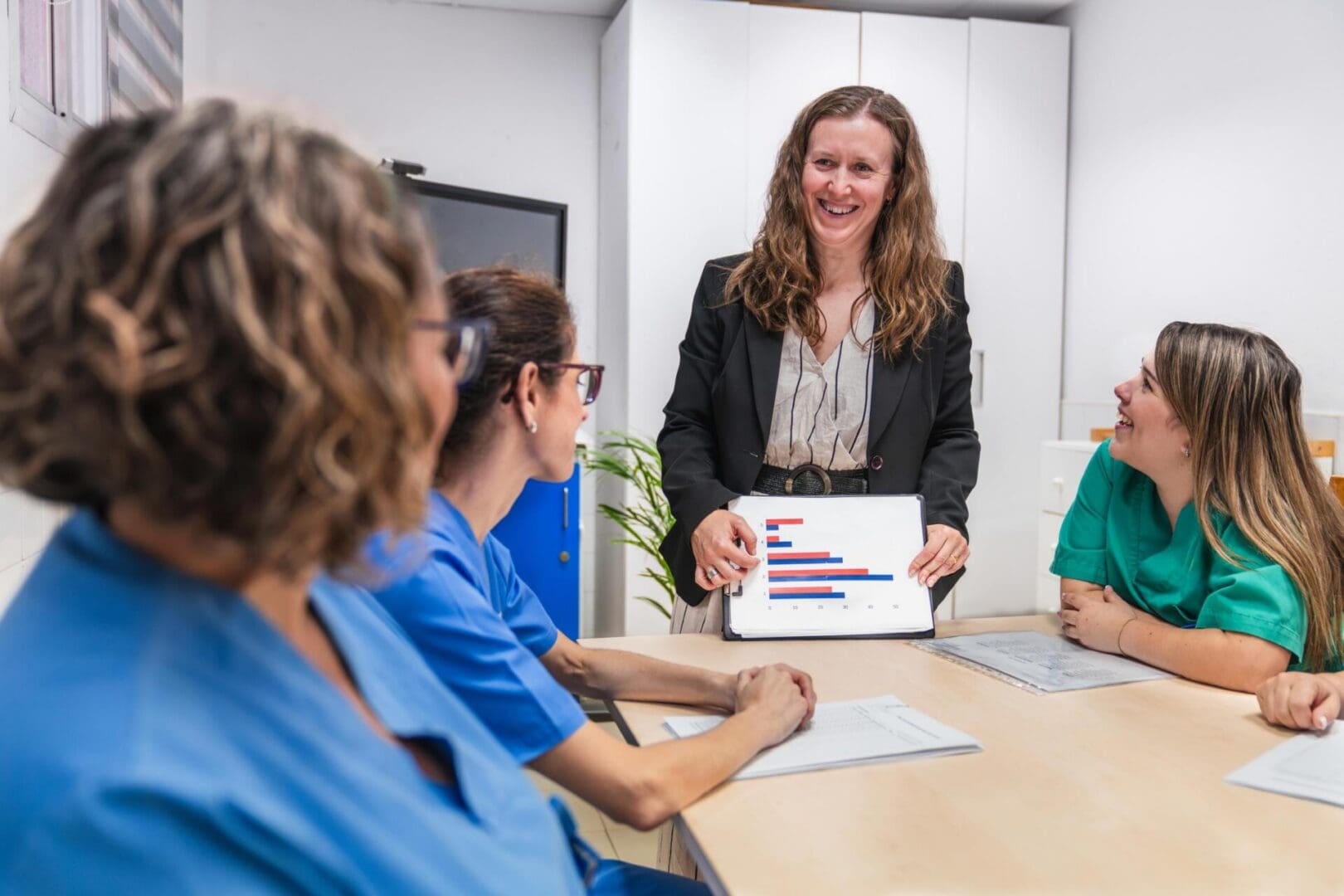 Healthcare professionals in a nursing home setting discuss patient care strategies. A leader presents data on a tablet, fostering collaboration and teamwork