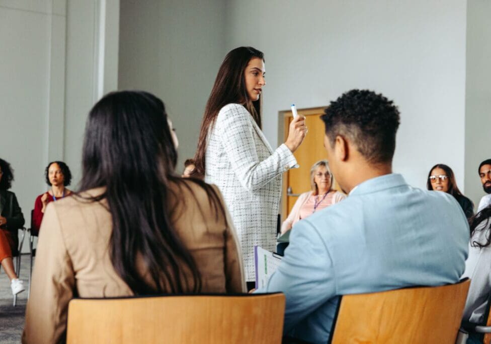 Woman speaking to a seated audience group.