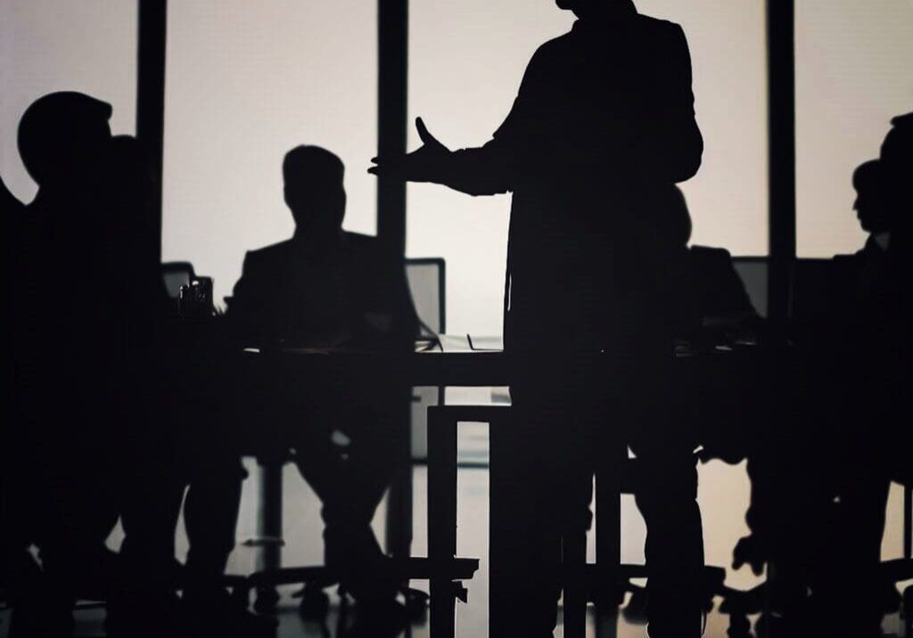 Silhouetted business meeting in dimly lit room.