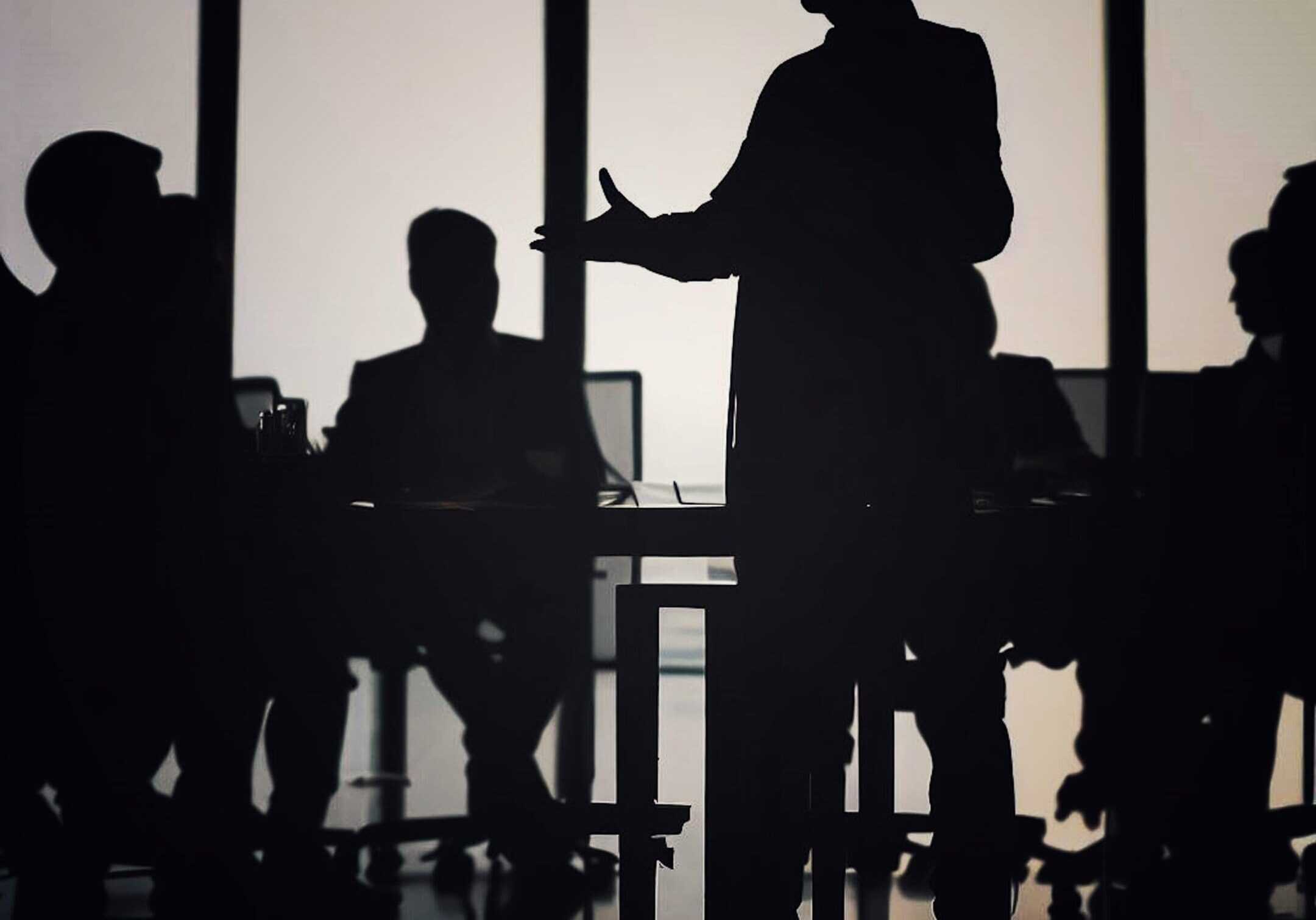 Silhouetted business meeting in dimly lit room.