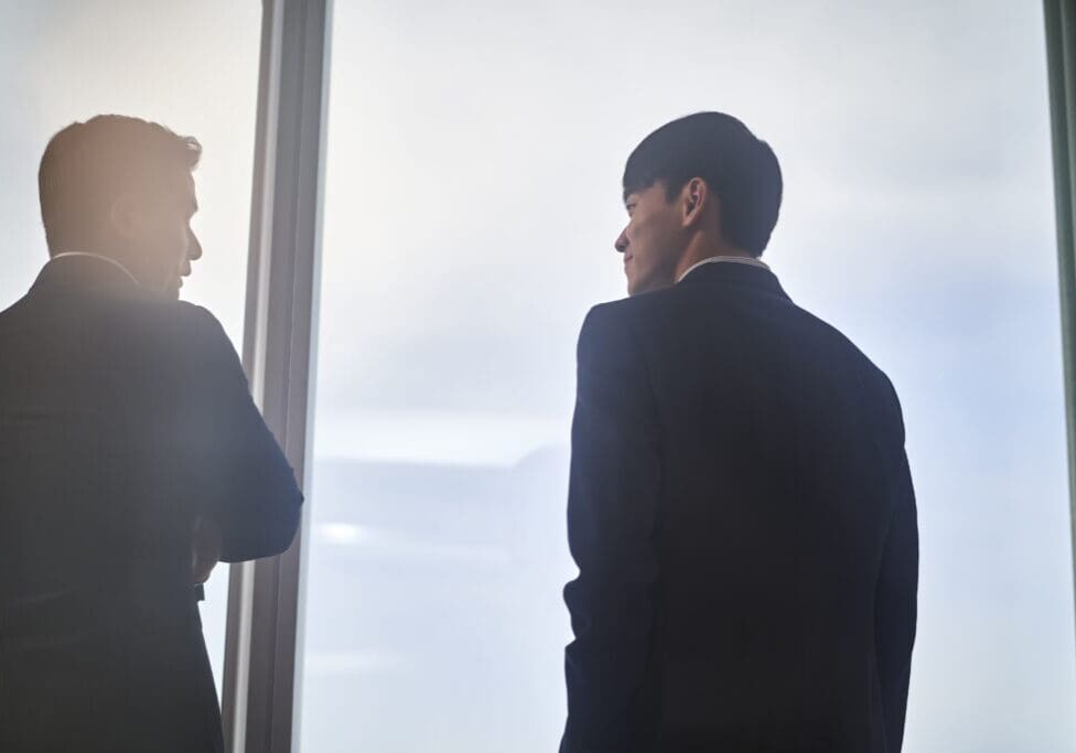 Two men in suits by a window.