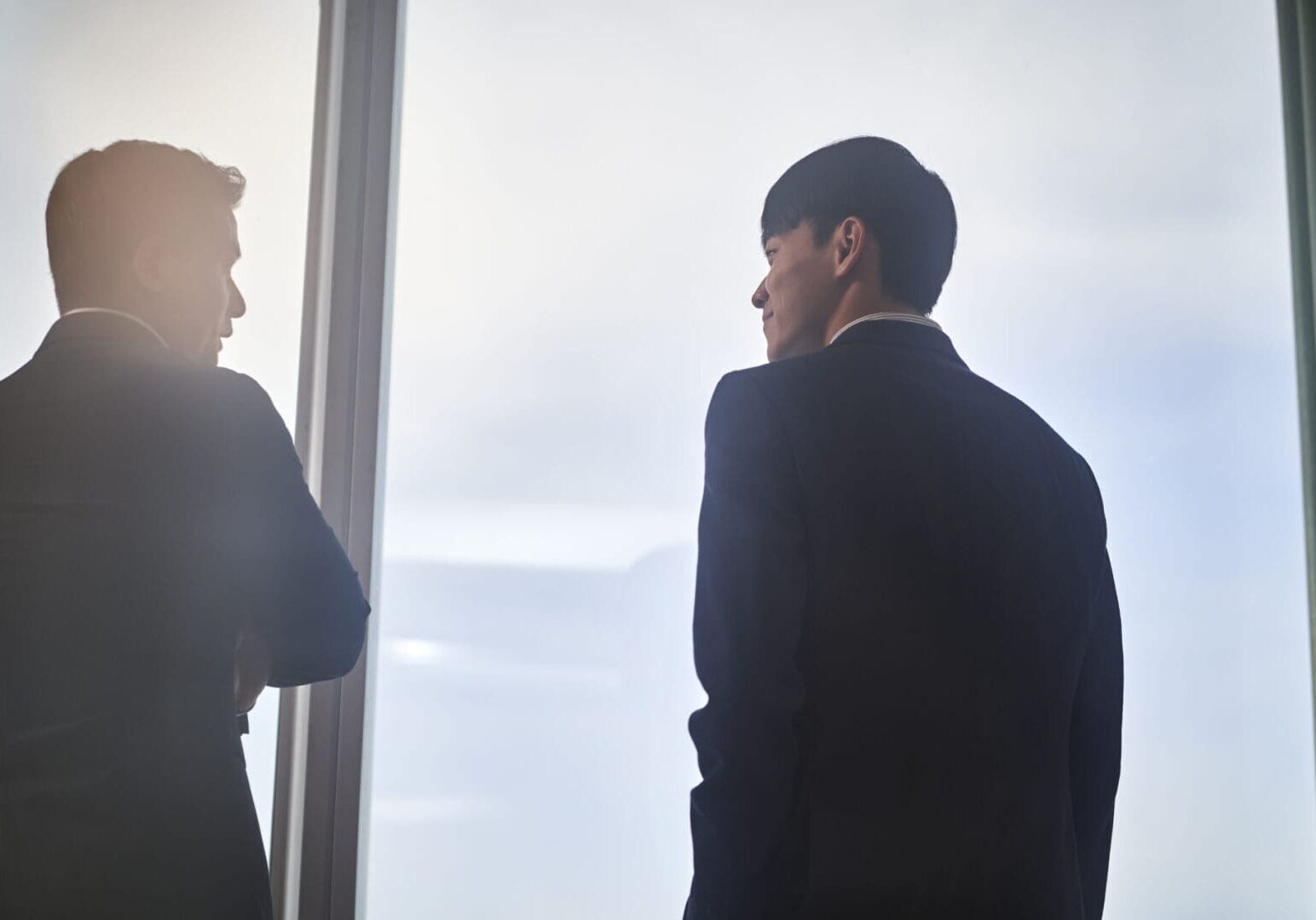 Two men in suits by a window.