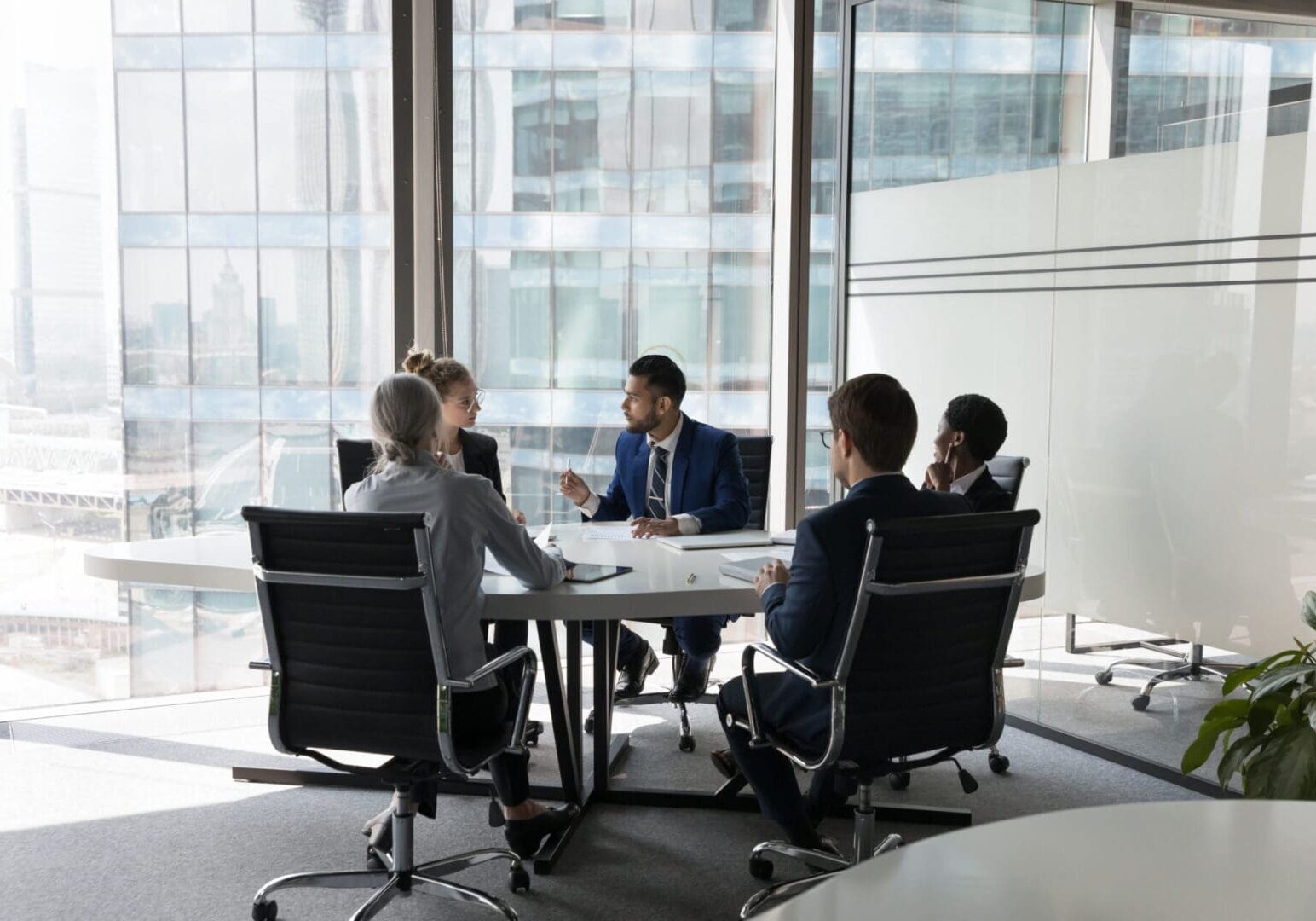 Serious team of professionals, five multi ethnic business people negotiating in modern boardroom, discuss project, consider contract terms and conditions, solve business. Formal meeting event concept