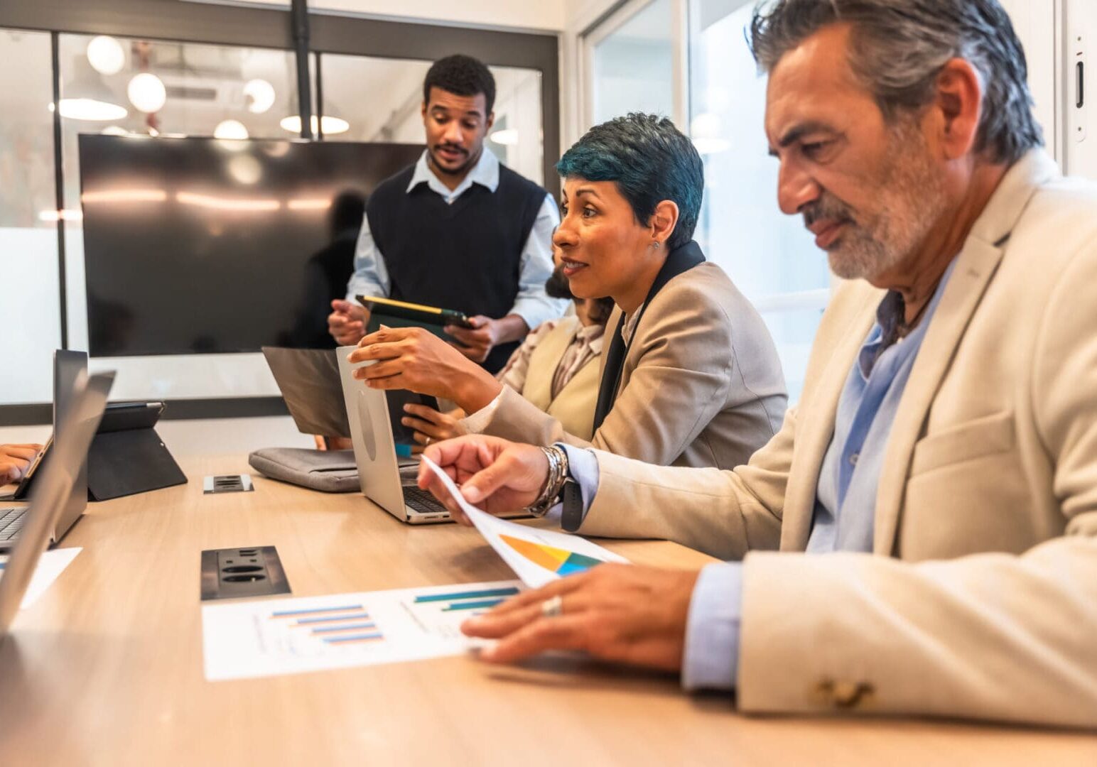 Diverse professionals collaborating in a modern conference room, reviewing charts and data on laptops and tablets, discussing strategy and teamwork for business growth and planning
