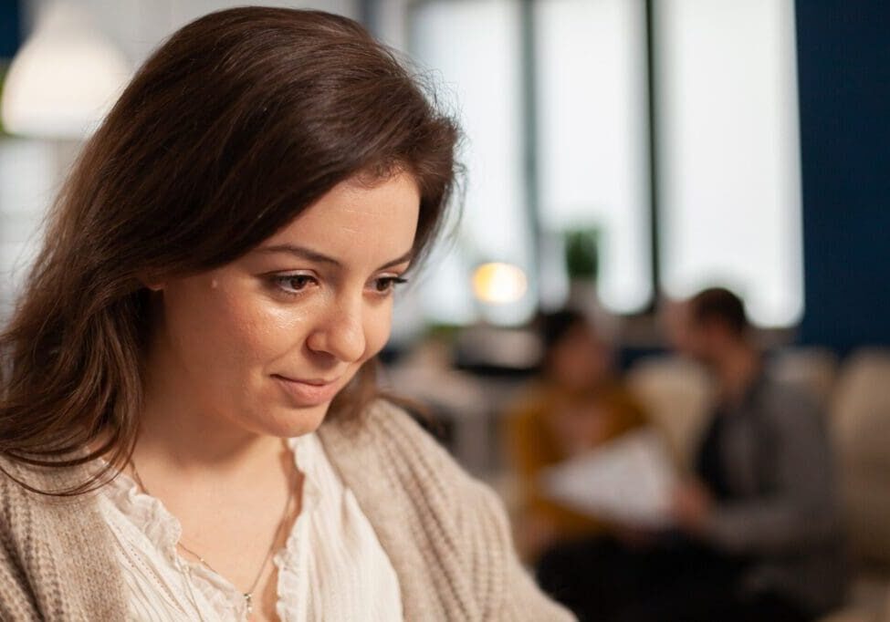 Smiling woman in focus, blurred background conversation.