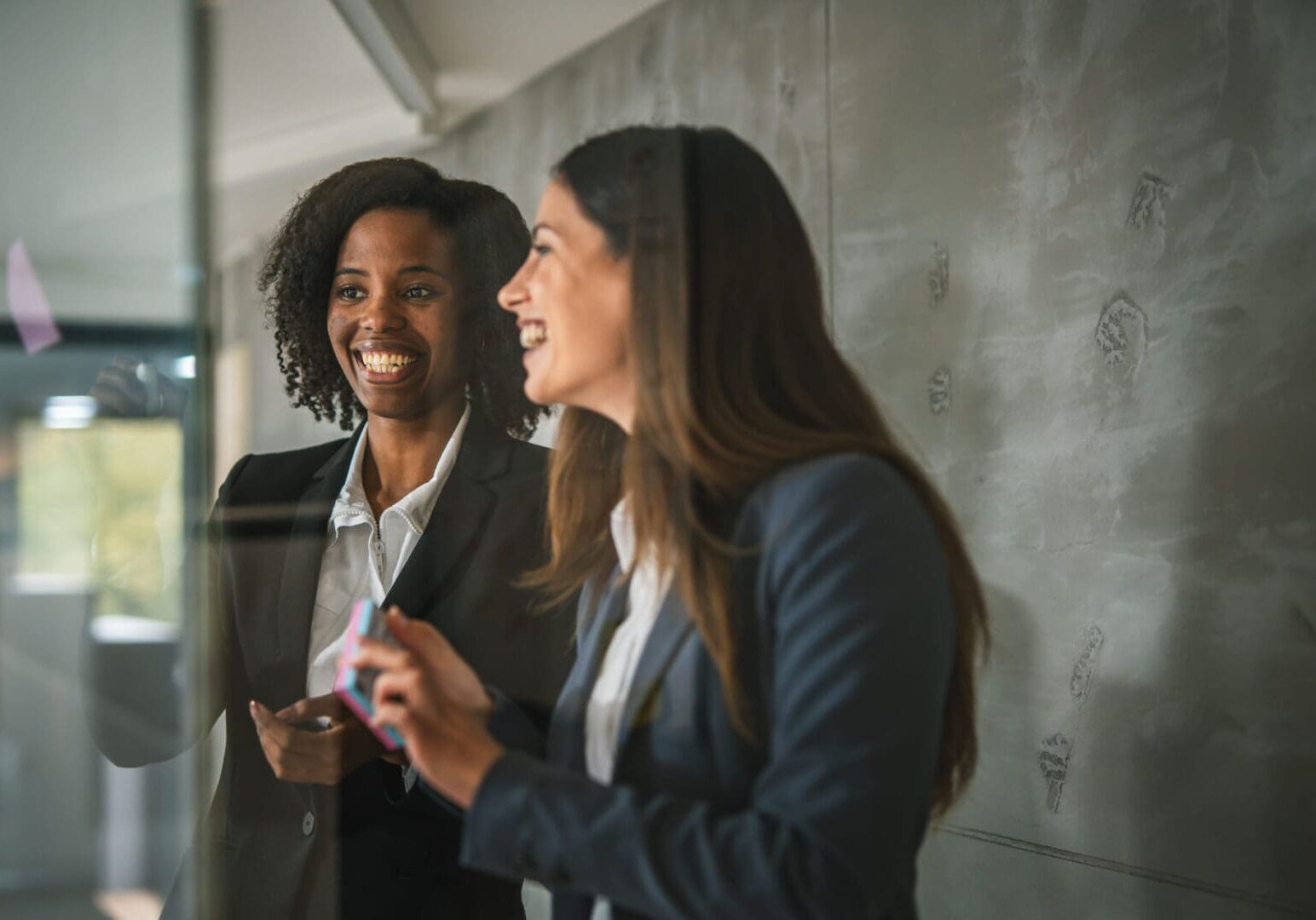 Two women discussing ideas on glass board.