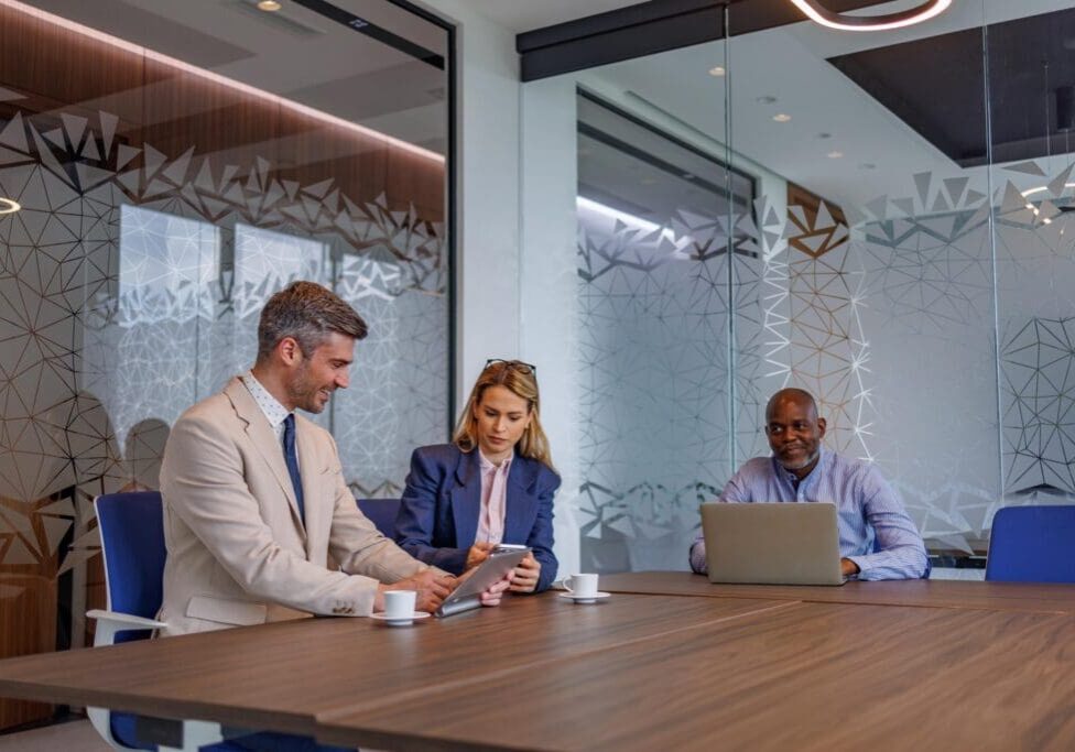 Diverse business professionals collaborating in a modern office meeting room, discussing strategy and using digital tablet during a corporate board session