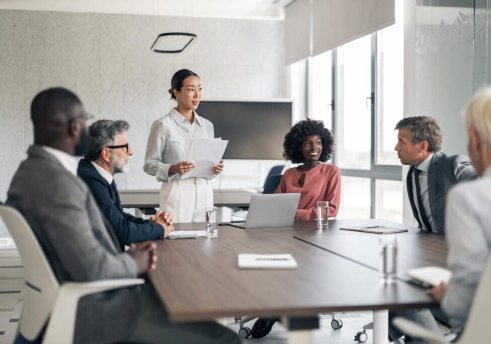 Young Asian business leader giving a presentation during a corporate meeting in a professional office environment, with diverse colleagues actively listening and engaging in discussion