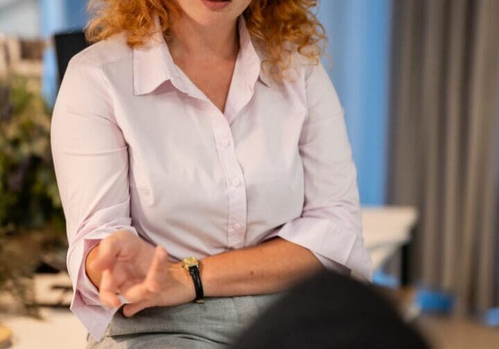 Red-haired woman wearing glasses gesturing while seated