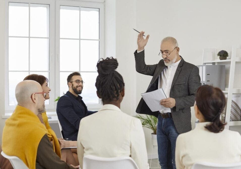 Experienced mentor communicating with people during lecture or business training. Coach sharing expertise with team of multiracial employees, teaching how to change mindset, inspiring to achieve more