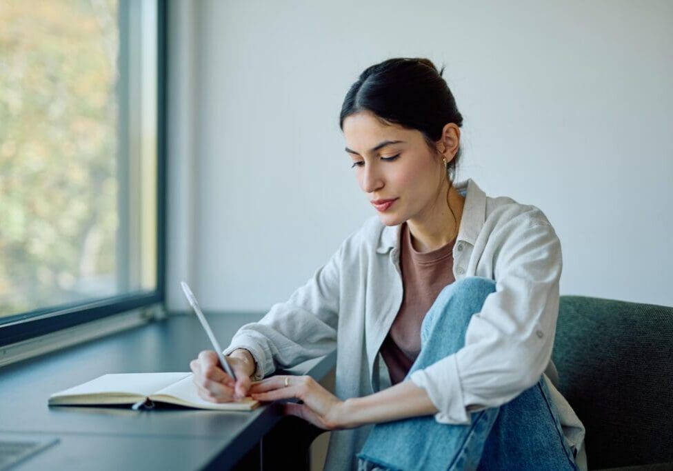 Woman writing notes at a bright windowsill