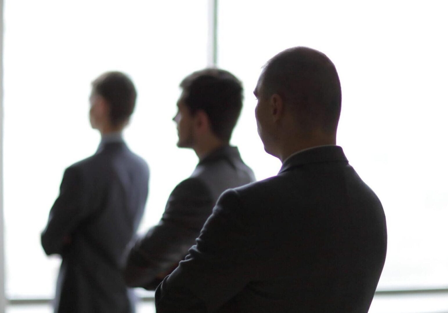 Three people in suits silhouetted against window
