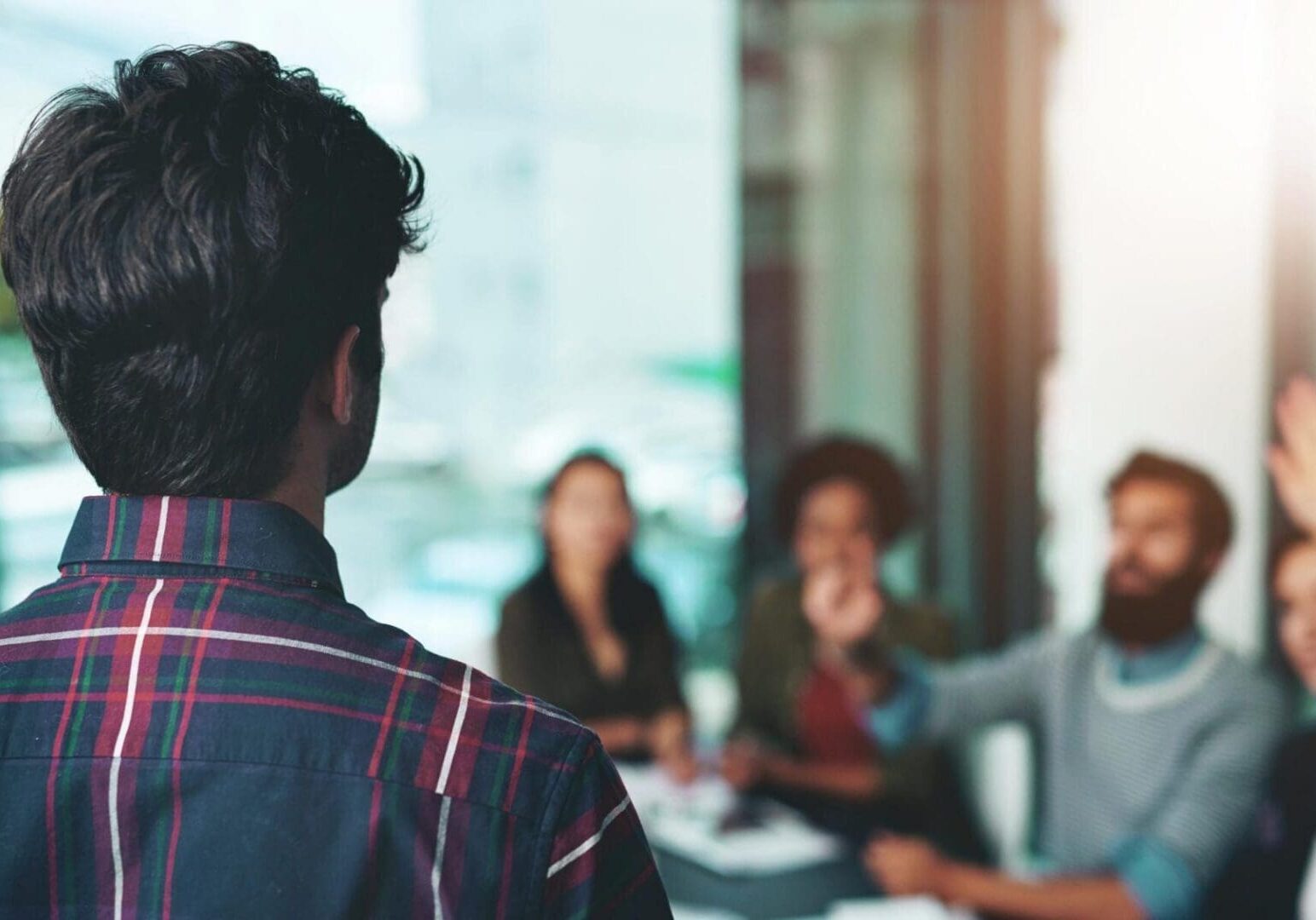 Man presenting to colleagues with raised hand