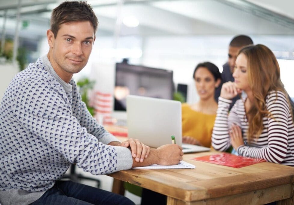 Man writing at desk with colleagues