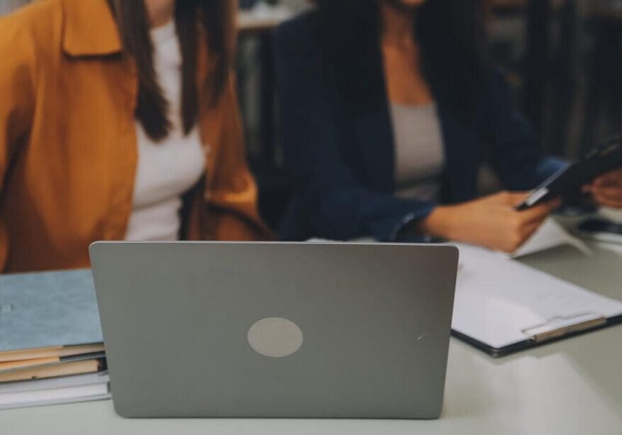 Laptop on desk with two people collaborating