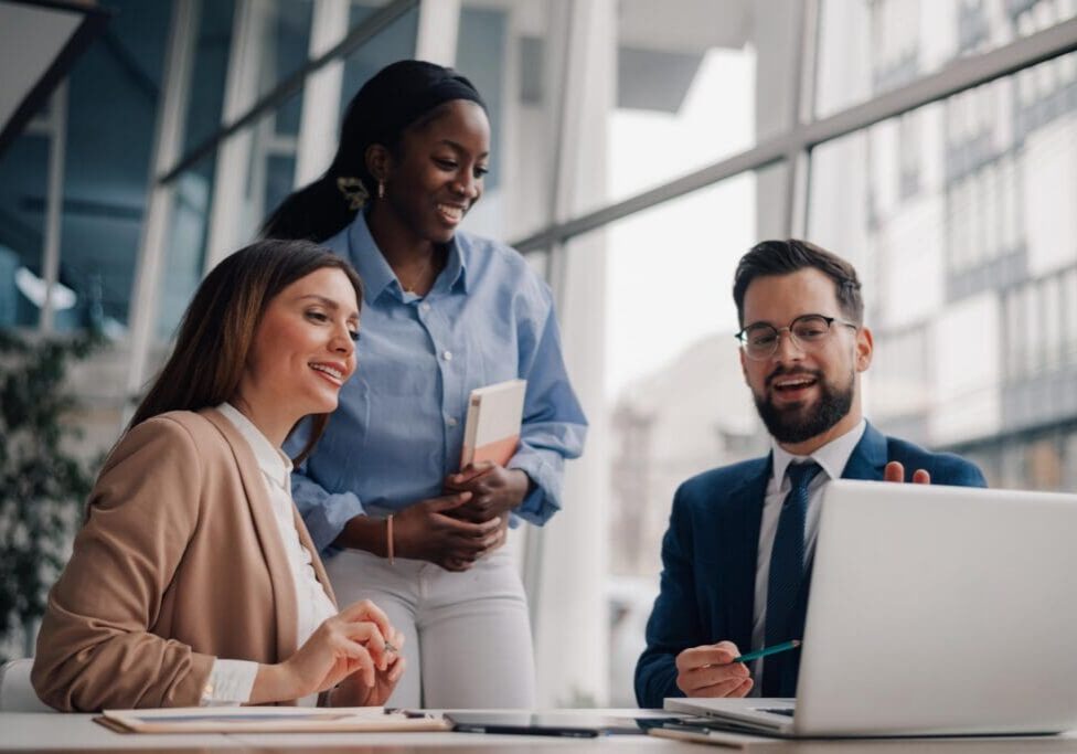 Three colleagues smiling while working at laptop