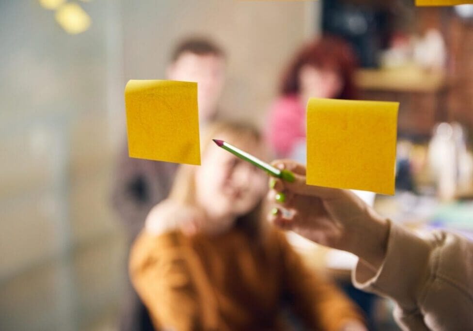 Green pencil pointing at yellow sticky notes