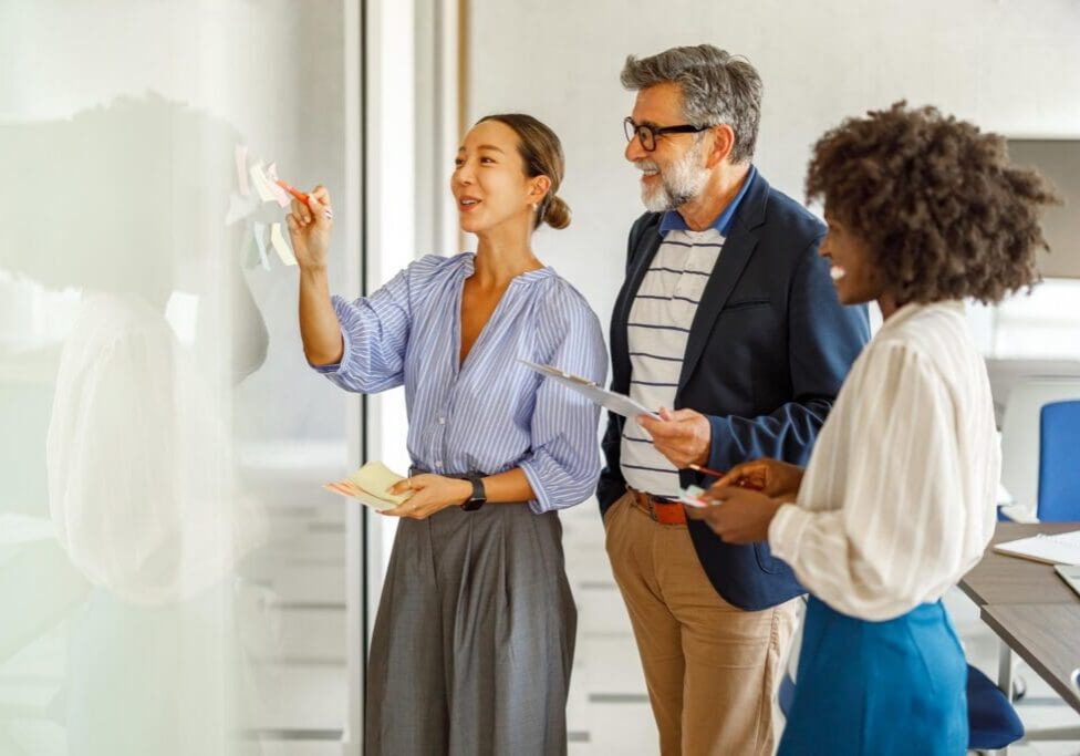 Three colleagues placing sticky notes on glass