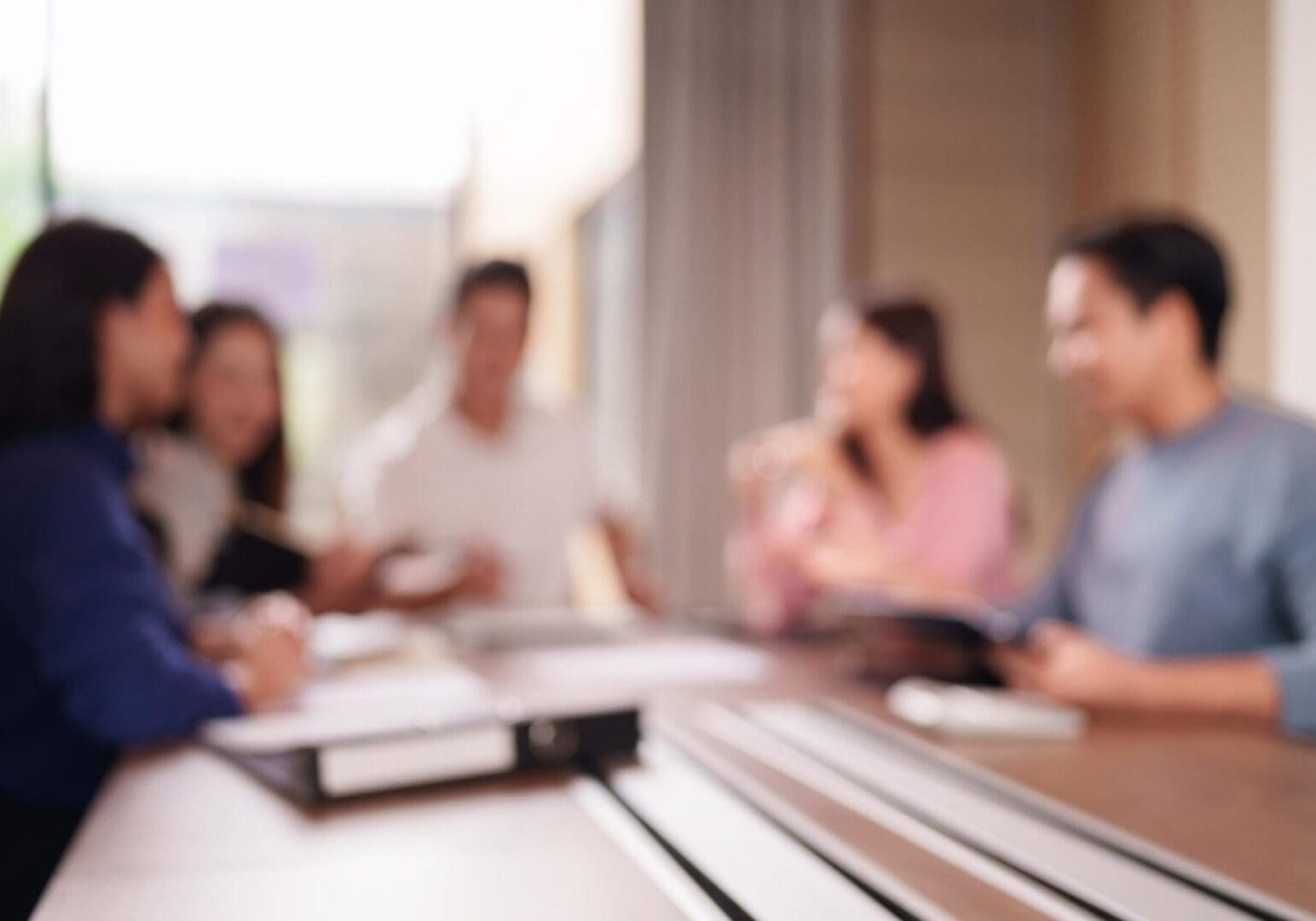 Abstract image of adult Asian professionals in a blurred conference room setting discussing important corporate plans and teamwork.