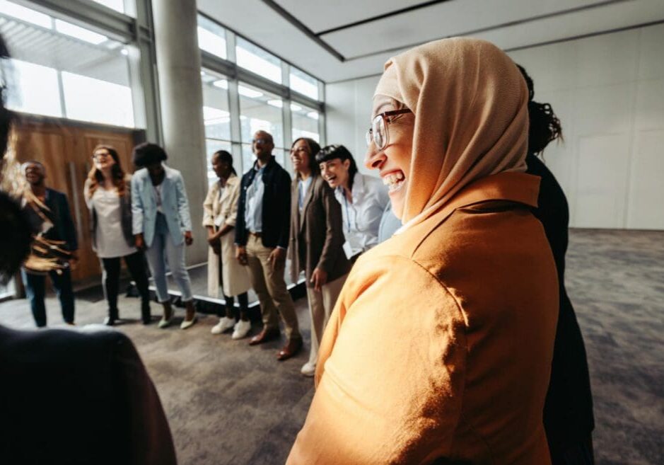 A diverse team engages in a bonding activity, with a Muslim woman laughing in a circle during a workshop.