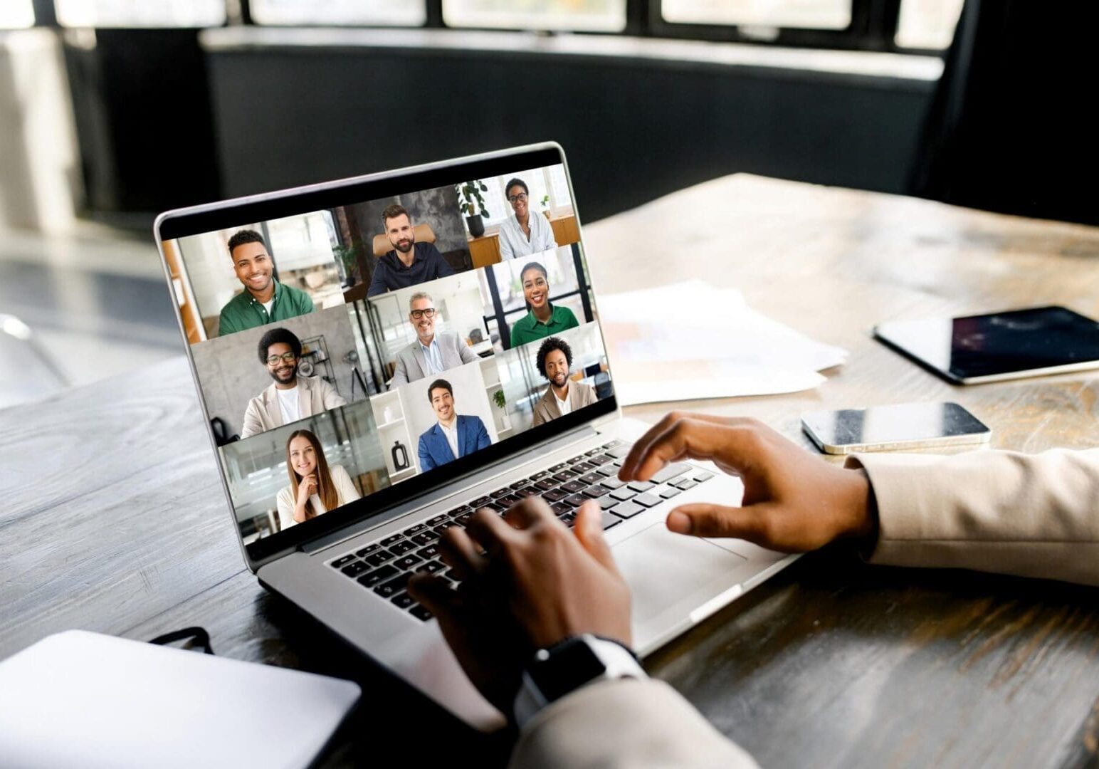 Young entrepreneur is shown in the midst of a cheerful virtual meeting, with a laptop screen displaying a gallery of friendly and diverse faces. Virtual meeting and video call concept