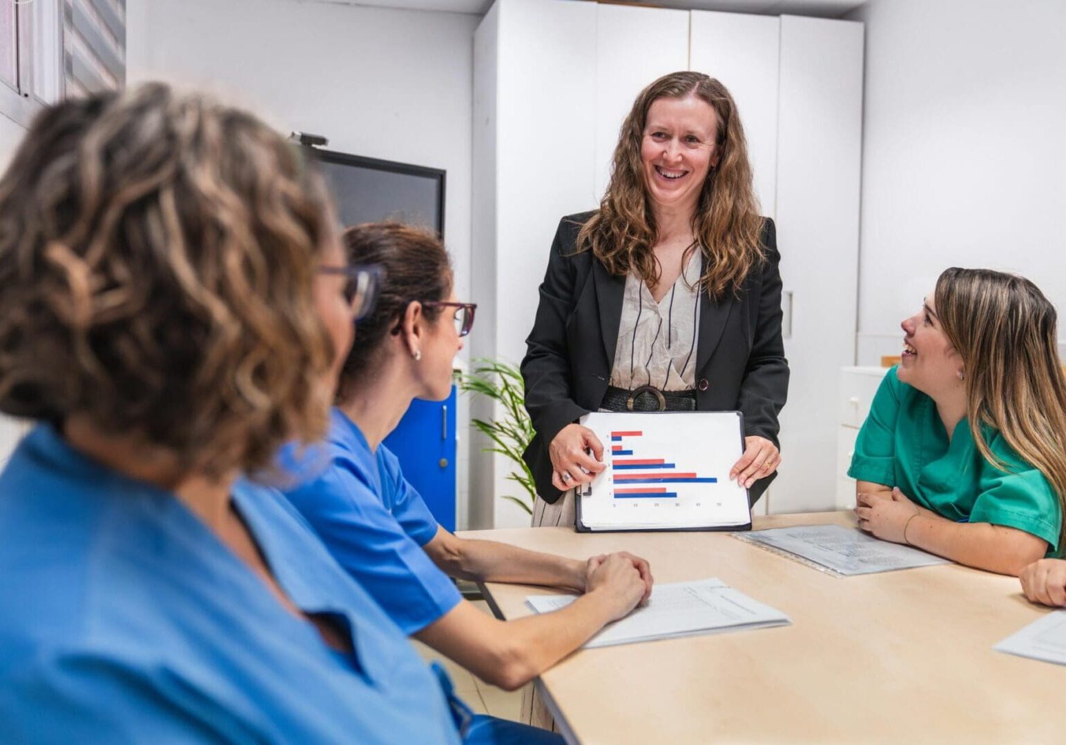 Healthcare professionals in a nursing home setting discuss patient care strategies. A leader presents data on a tablet, fostering collaboration and teamwork