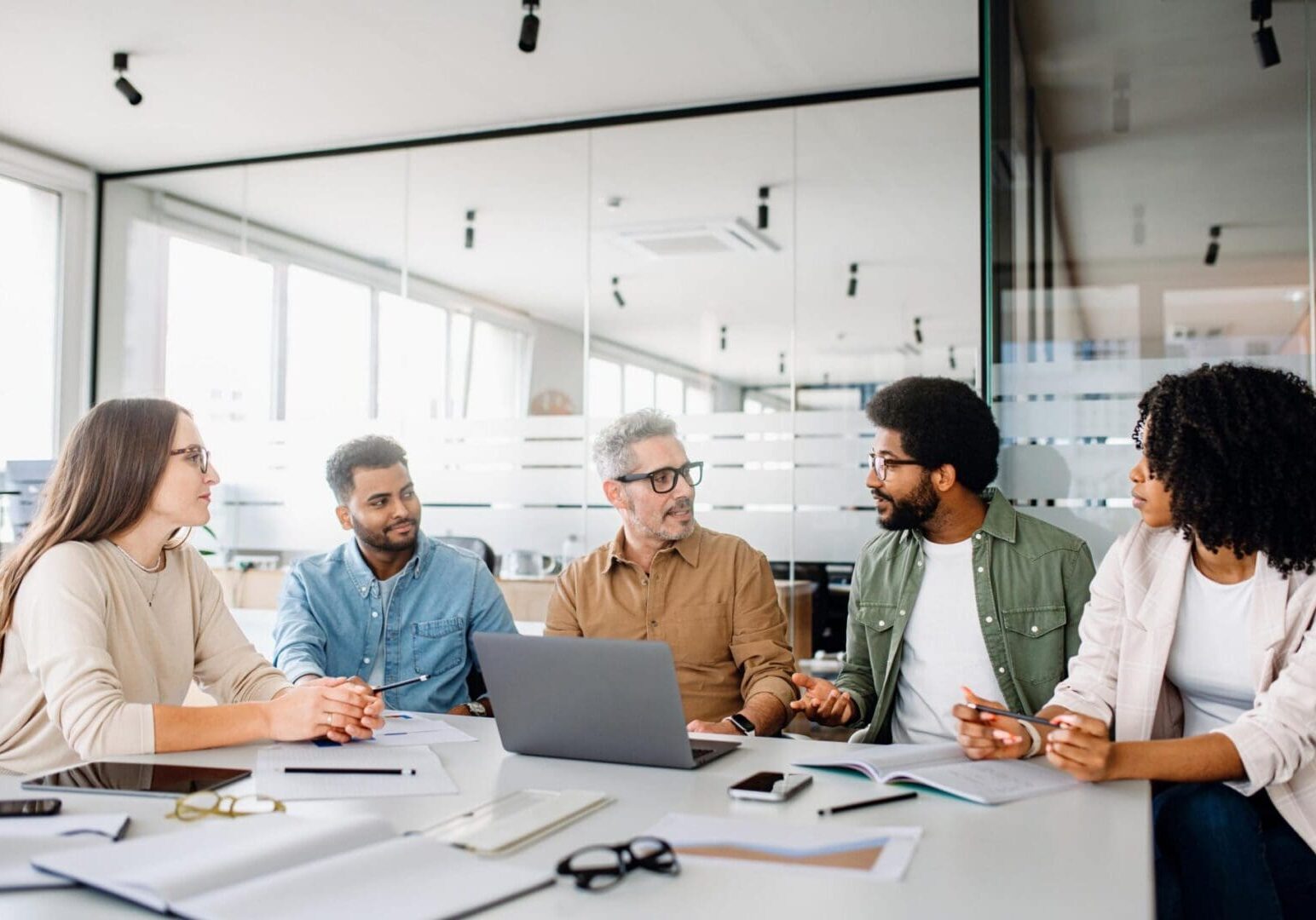 A diverse office team is engaged in a strategic meeting, with a senior colleague leading discussion, illustrating a productive and inclusive workplace. Colleagues engage in a lively exchange of ideas