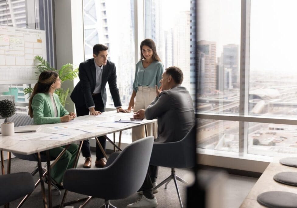 Group of four professionals engaged in srategic business planning meeting in high-rise office with panoramic city view. Team brainstorming ideas, making important decisions. Seminar, briefing event