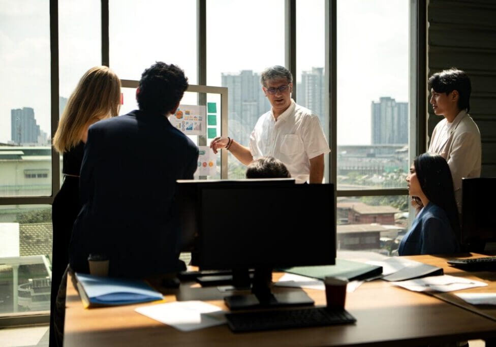 Business leader presenting information to a team during a meeting, explaining charts and reports while colleagues listen in a professional office setting