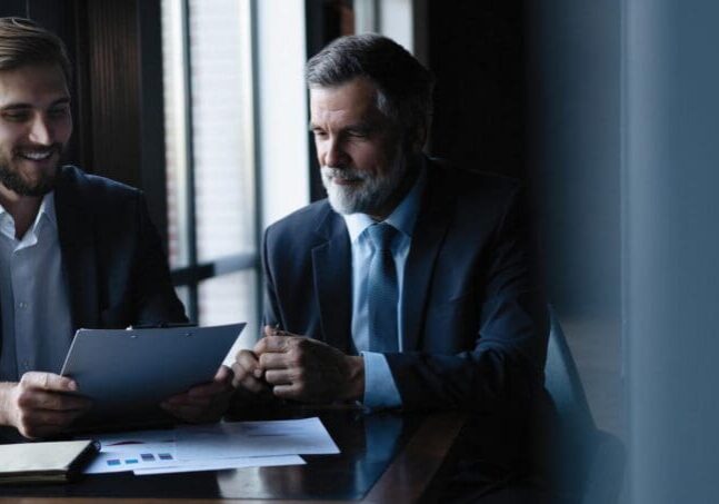 Good deal. Senior and junior businessman discuss something during their meeting, office background
