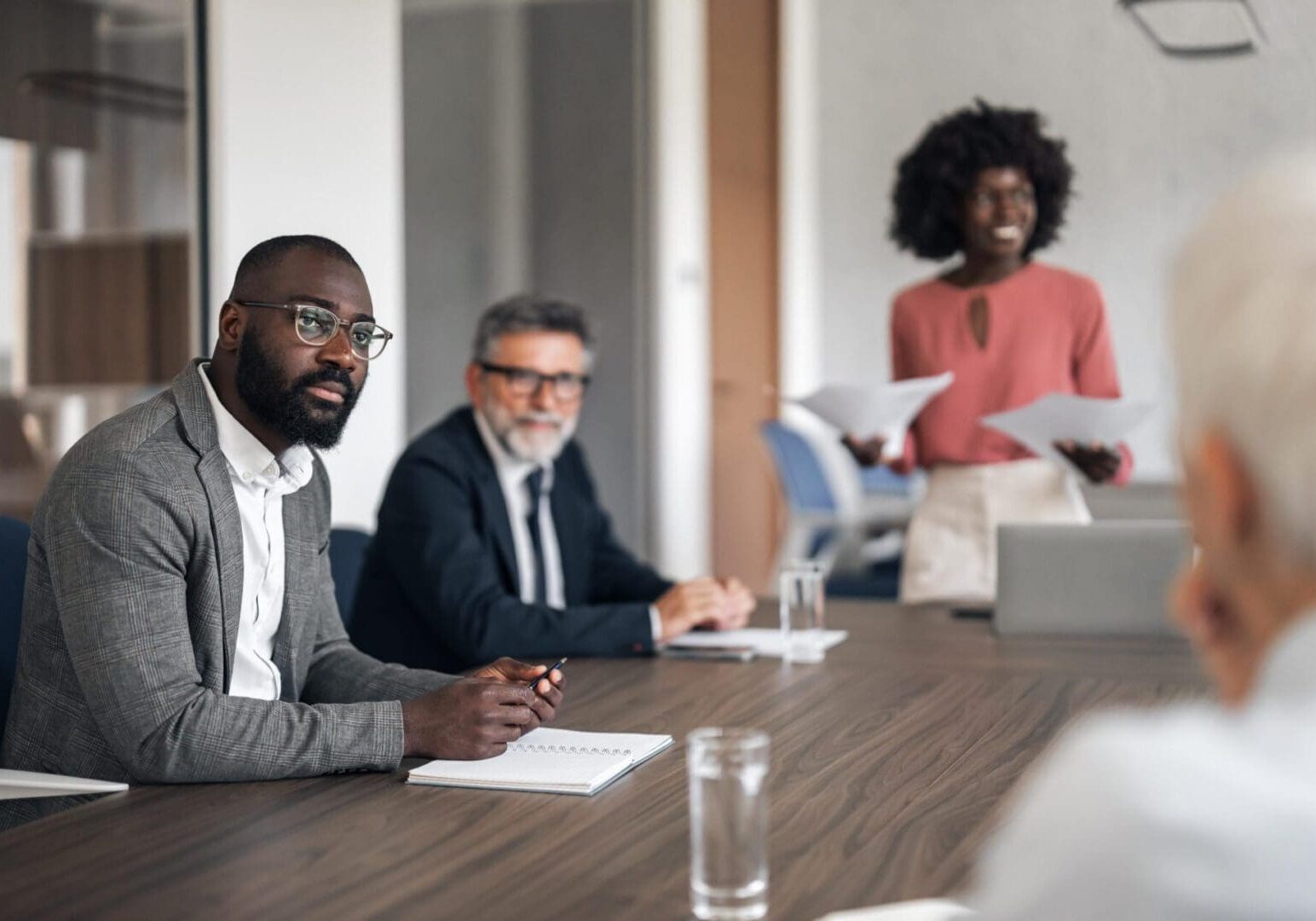 Diverse business team collaborating during a corporate meeting in a modern office, listening to an African American woman presenting while sharing ideas and strategy